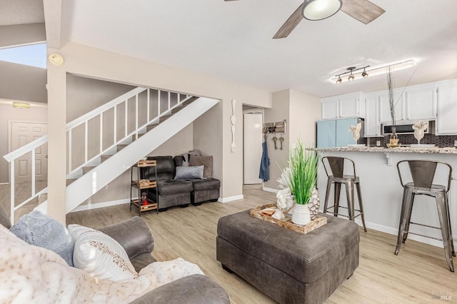 living room with stairway, ceiling fan, baseboards, and light wood-type flooring