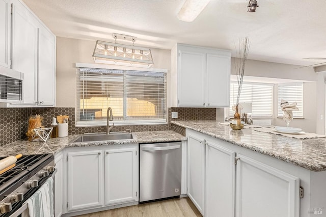 kitchen with stainless steel appliances, a peninsula, a sink, white cabinetry, and decorative backsplash