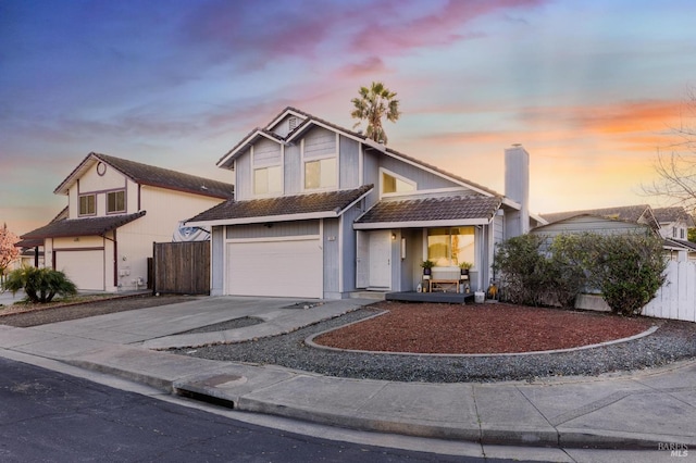 traditional home featuring a tiled roof, a chimney, concrete driveway, fence, and a garage