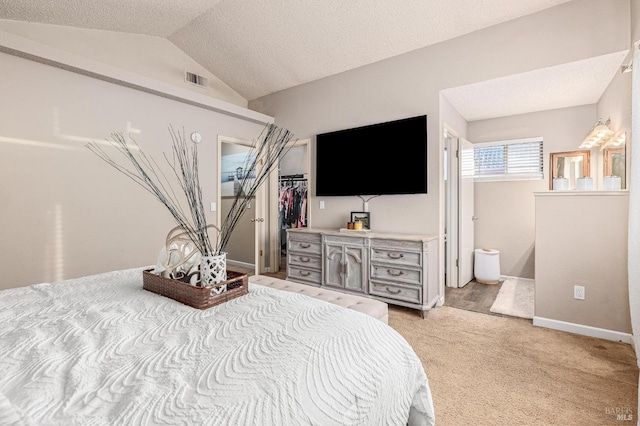 bedroom featuring ensuite bathroom, a walk in closet, light carpet, lofted ceiling, and visible vents