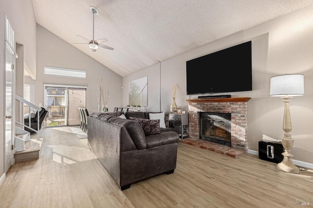 living area with a textured ceiling, a ceiling fan, wood finished floors, a brick fireplace, and high vaulted ceiling