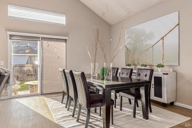 dining area with baseboards, wood finished floors, and high vaulted ceiling