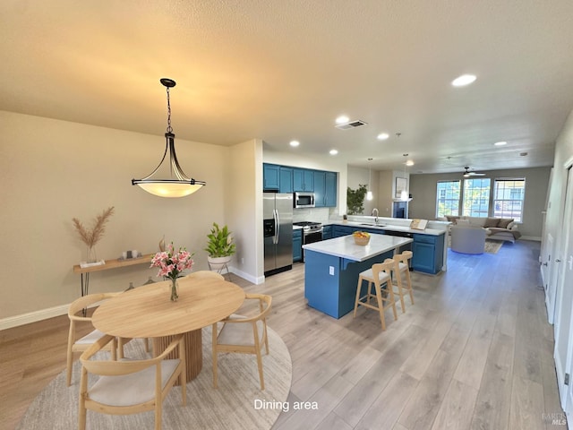 kitchen featuring blue cabinets, stainless steel appliances, a peninsula, light countertops, and light wood finished floors