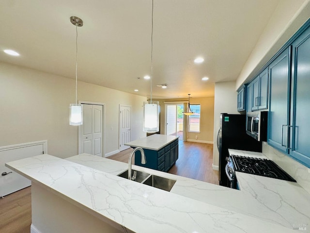 kitchen featuring light wood-style flooring, a sink, blue cabinetry, a center island, and stainless steel microwave