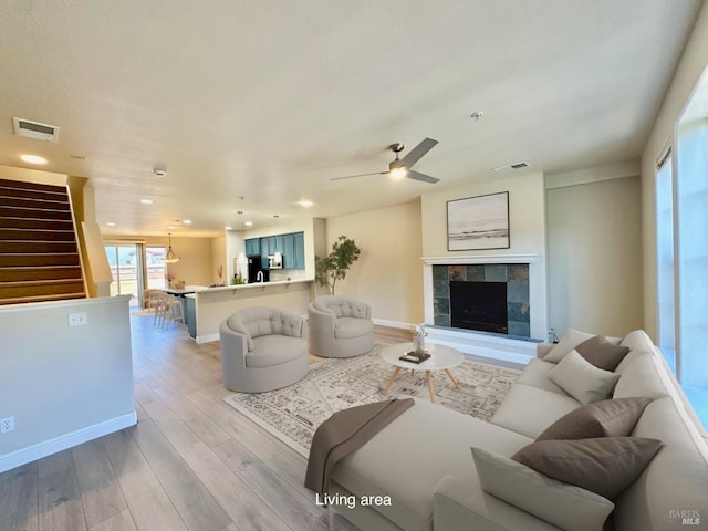 living area featuring light wood-style floors, a tile fireplace, visible vents, and baseboards