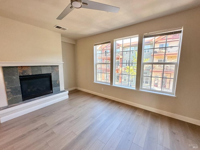 unfurnished living room with baseboards, visible vents, wood finished floors, and a tile fireplace