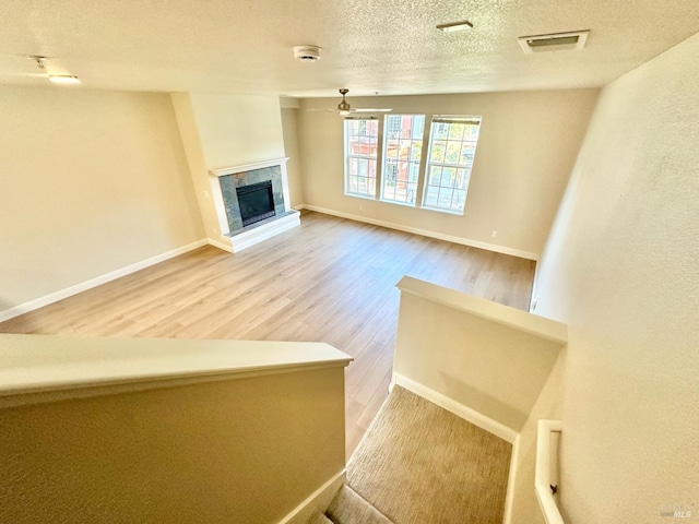 unfurnished living room with a textured ceiling, a premium fireplace, visible vents, baseboards, and light wood-style floors