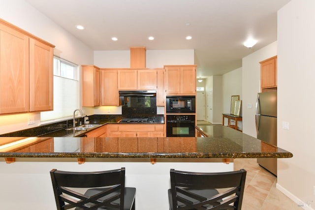 kitchen with a peninsula, under cabinet range hood, black appliances, light brown cabinets, and a sink