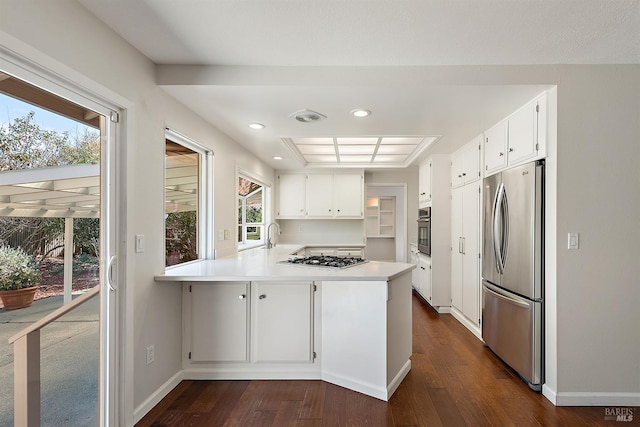 kitchen with a peninsula, white cabinets, dark wood-type flooring, and stainless steel appliances