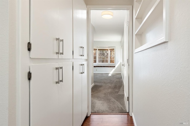 corridor featuring dark wood-type flooring, baseboards, and dark carpet