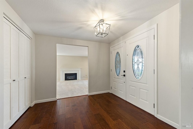 foyer with dark wood-style floors, a notable chandelier, a fireplace, and baseboards