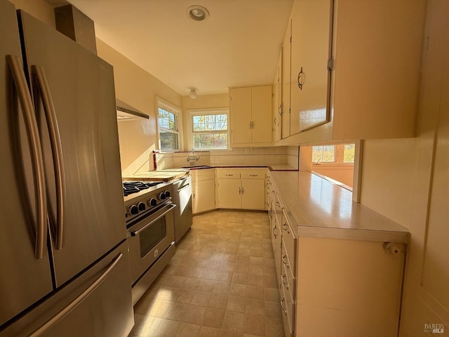 kitchen with a sink, white cabinetry, stainless steel appliances, wall chimney exhaust hood, and light countertops