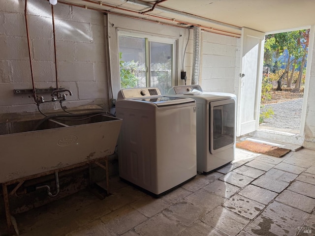 washroom with a sink, concrete block wall, washing machine and dryer, and laundry area