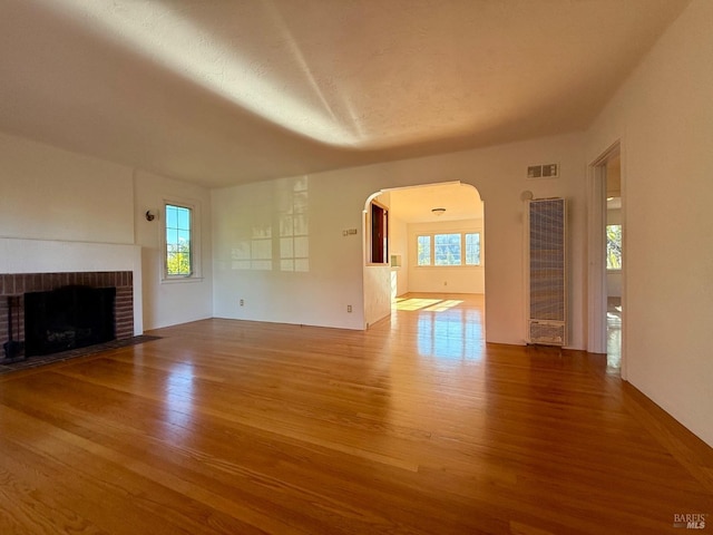 unfurnished living room featuring arched walkways, visible vents, a fireplace, and wood finished floors