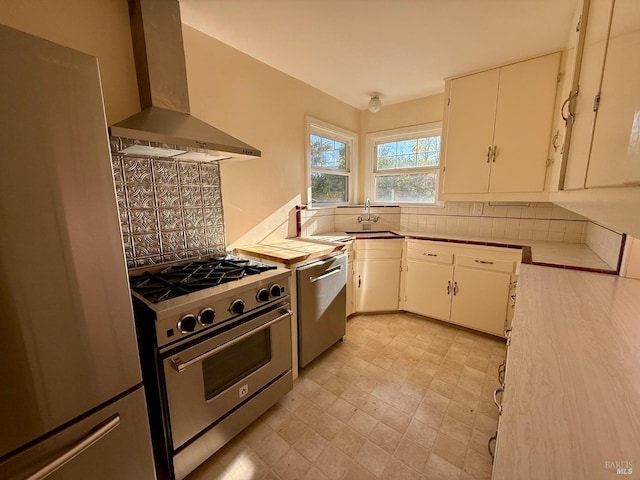 kitchen featuring decorative backsplash, appliances with stainless steel finishes, wall chimney exhaust hood, and a sink