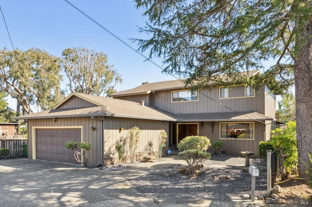 traditional home featuring an attached garage, driveway, roof with shingles, and fence