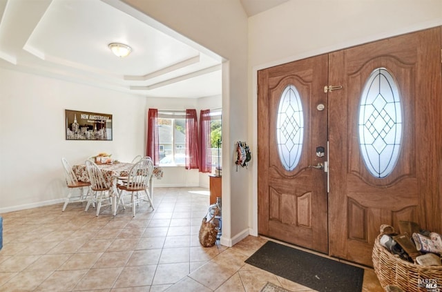 entrance foyer featuring light tile patterned flooring, a raised ceiling, and baseboards
