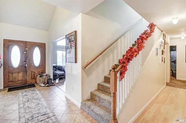 foyer entrance with light tile patterned flooring, stairway, baseboards, and vaulted ceiling