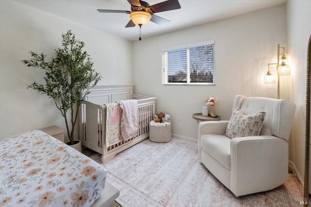 bedroom featuring baseboards, a nursery area, and ceiling fan