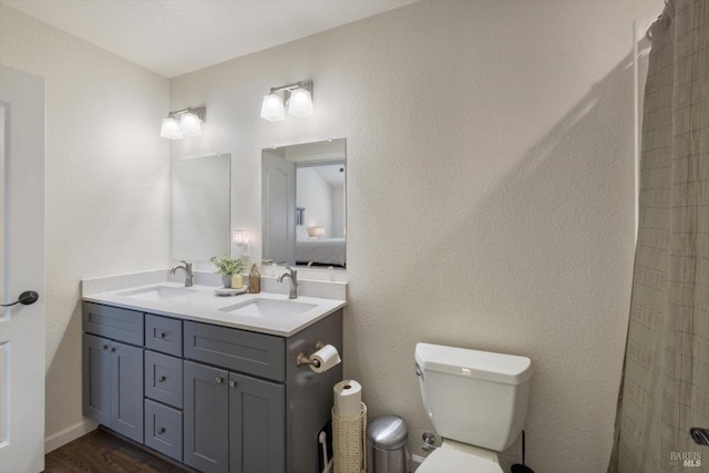 bathroom featuring double vanity, toilet, wood finished floors, and a sink