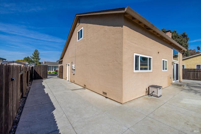 view of side of property featuring stucco siding, a chimney, a patio, and fence