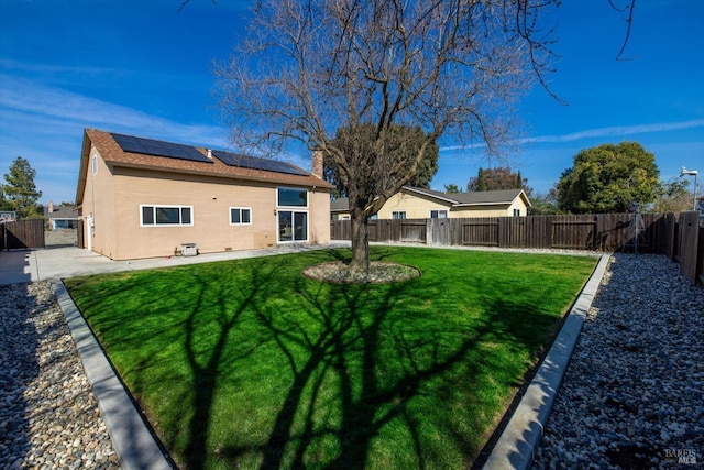 rear view of property featuring roof mounted solar panels, a yard, a fenced backyard, a patio area, and a gate