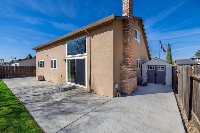 rear view of property featuring a patio, a chimney, stucco siding, an outdoor structure, and a storage unit