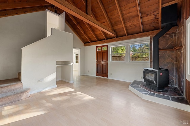 unfurnished living room with stairs, beamed ceiling, wood finished floors, and a wood stove