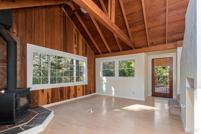 unfurnished living room with beamed ceiling, wood finished floors, wood walls, wood ceiling, and a wood stove