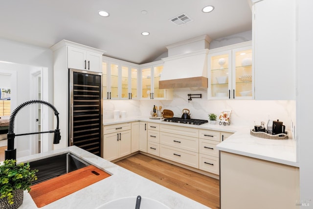 kitchen with visible vents, a sink, premium range hood, wine cooler, and gas cooktop