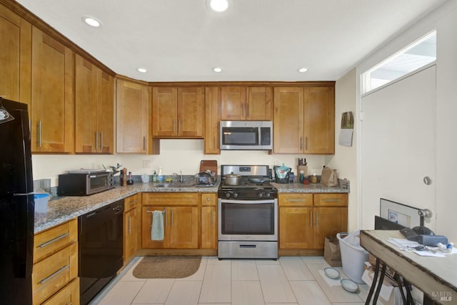 kitchen featuring stone counters, brown cabinets, black appliances, and a sink