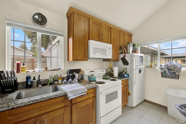 kitchen featuring vaulted ceiling, light stone counters, brown cabinetry, white appliances, and a sink