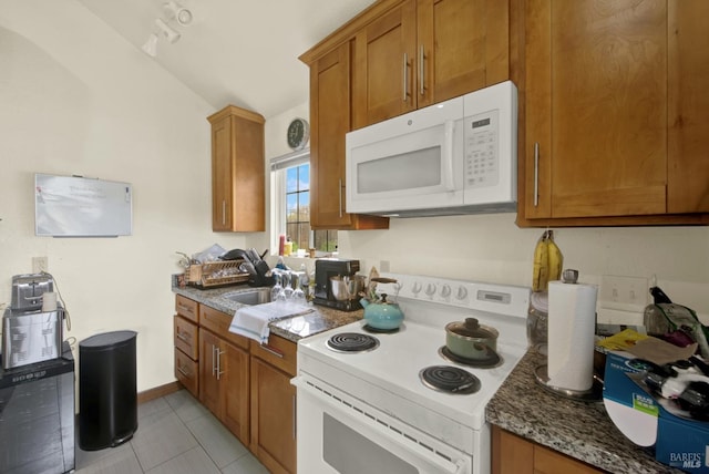 kitchen featuring white appliances, light tile patterned floors, brown cabinetry, dark stone counters, and a sink