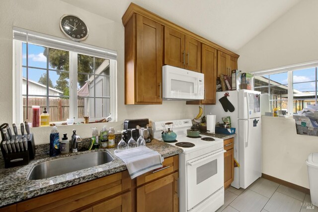 kitchen with white appliances, light stone countertops, brown cabinetry, lofted ceiling, and a sink