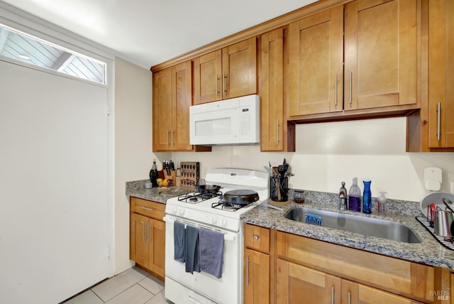 kitchen with white appliances, light tile patterned floors, brown cabinetry, light stone countertops, and a sink