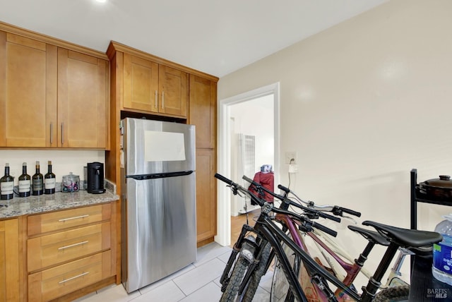 kitchen featuring light tile patterned floors, light stone counters, brown cabinets, and freestanding refrigerator