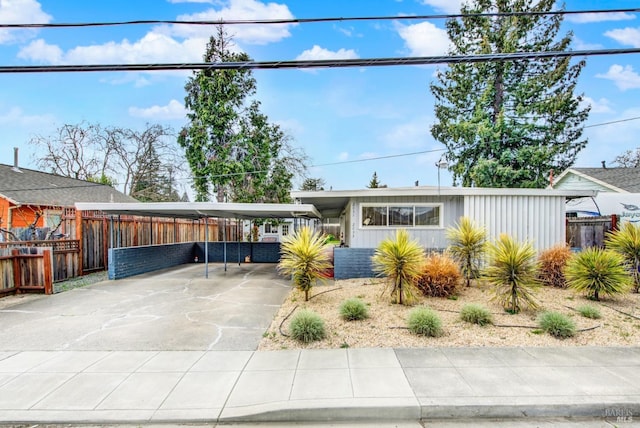 mid-century modern home featuring a carport, concrete driveway, and fence