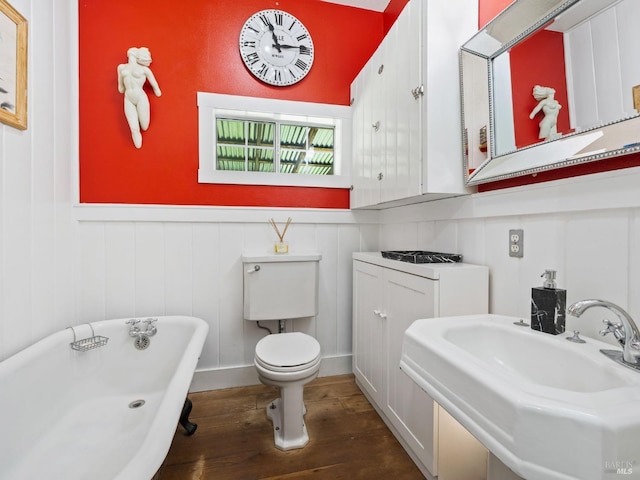 full bathroom with wood finished floors, a soaking tub, a sink, wainscoting, and toilet