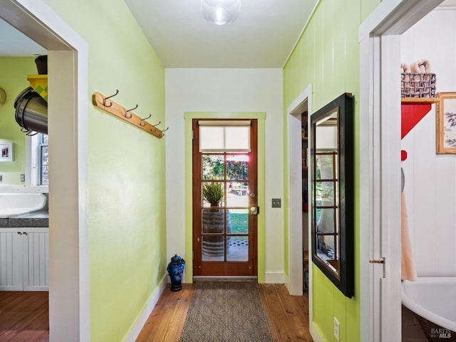 doorway to outside featuring wood finished floors, baseboards, and a sink