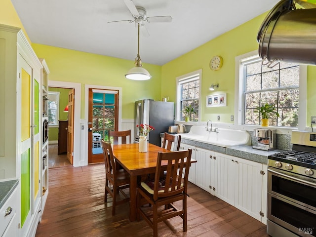 dining room with dark wood finished floors, a ceiling fan, and wainscoting