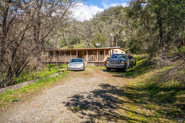 view of front facade with a wooded view, covered porch, and dirt driveway