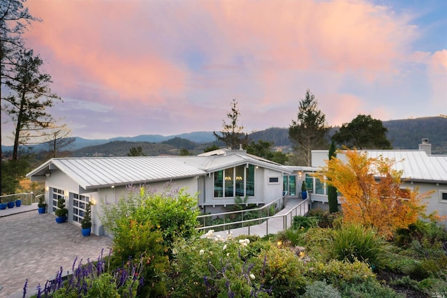 back of property at dusk featuring a standing seam roof, decorative driveway, fence, a mountain view, and metal roof