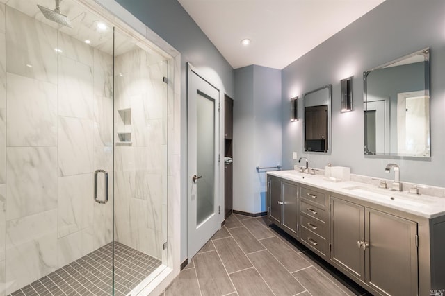 full bath with double vanity, a shower stall, baseboards, and a sink