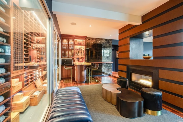 interior space featuring wood finished floors, beam ceiling, indoor bar, and a glass covered fireplace