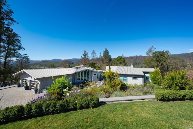 back of house with a lawn, a garage, driveway, a mountain view, and metal roof