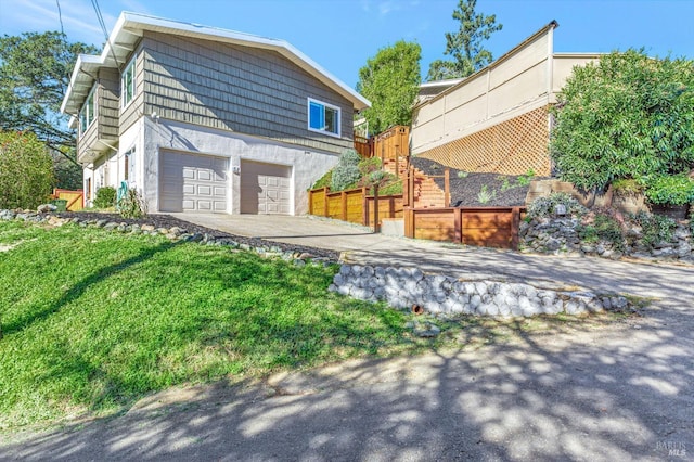 view of side of property featuring a garage, concrete driveway, stucco siding, and stairway