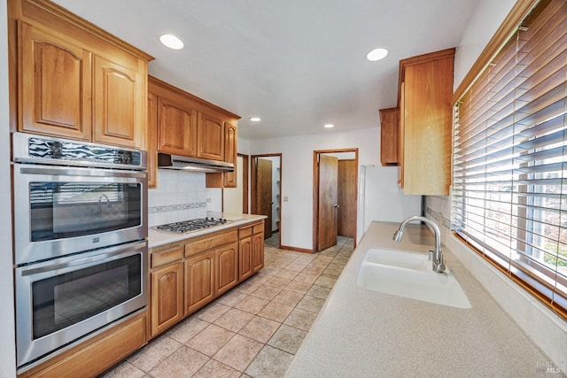 kitchen featuring light countertops, under cabinet range hood, appliances with stainless steel finishes, and a sink