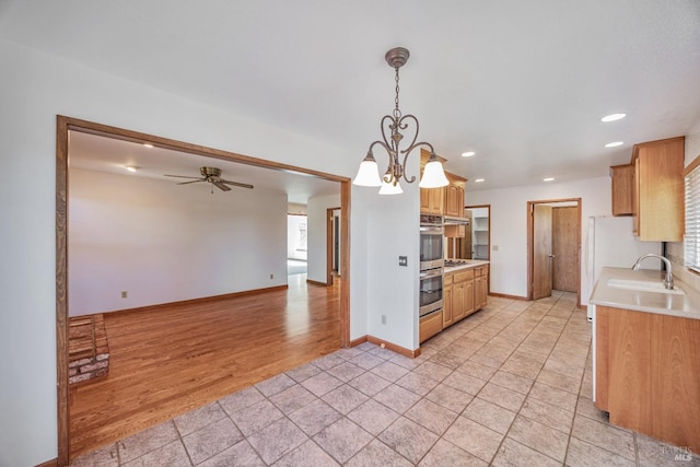 kitchen featuring light wood-style flooring, a ceiling fan, a sink, stainless steel double oven, and light countertops