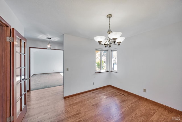 unfurnished room with visible vents, an inviting chandelier, baseboards, and wood finished floors