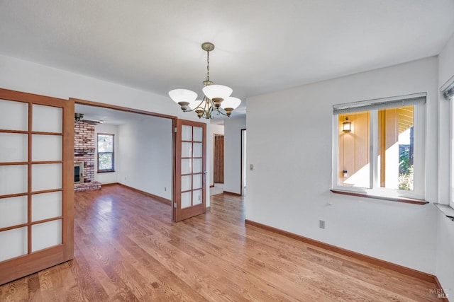 unfurnished room featuring baseboards, a chandelier, light wood-style flooring, a fireplace, and french doors